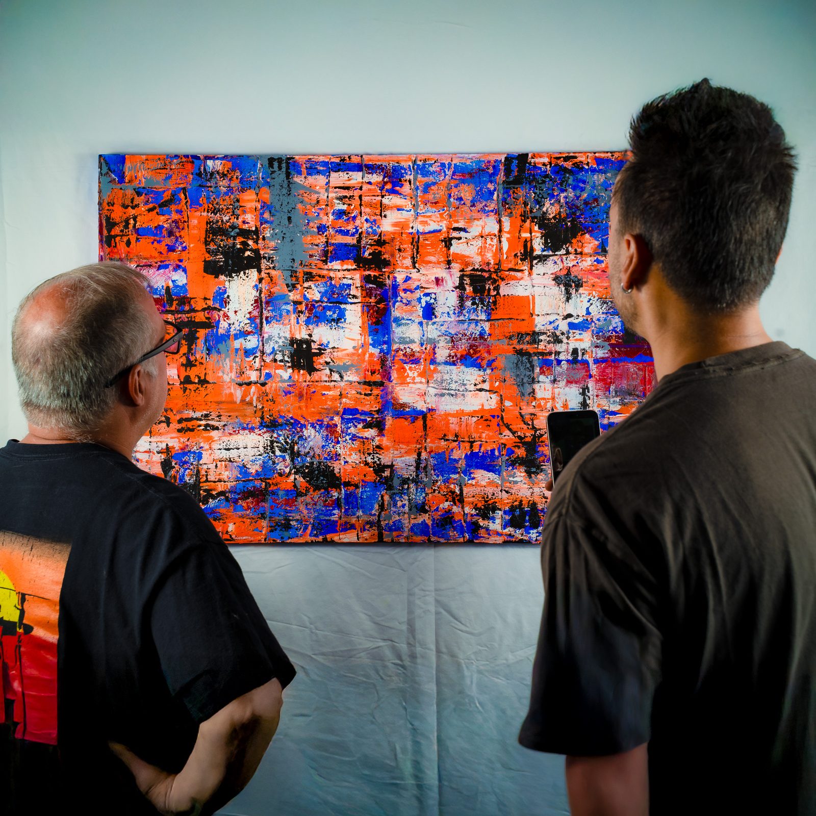 Two people studying a large orange and blue abstract painting by Michael Cababe during the catalog shoot