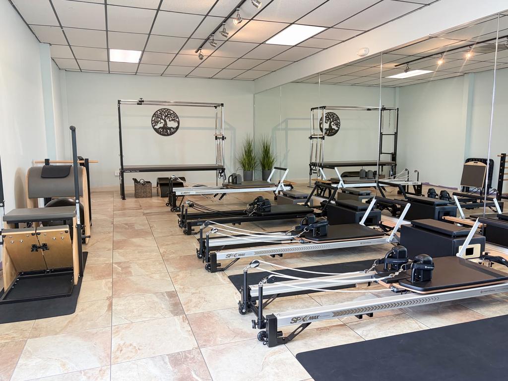 The studio's Reformer room, a row of Reformers facing a Cadillac and a wall of mirrors