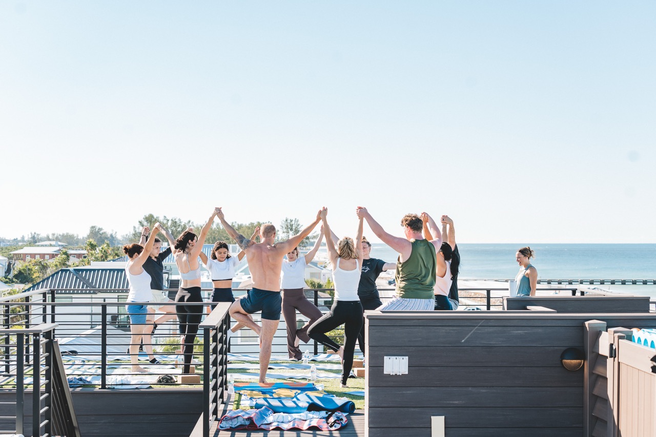 Wedding party in tree pose with linked arms against the gulf horizon, Bradenton Beach rooftop
